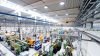 Imagen de una fábrica grande y moderna iluminada por varias campanas LED suspendidas del techo, mostrando la amplia cobertura y la intensidad de la luz que proporcionan en un entorno industrial